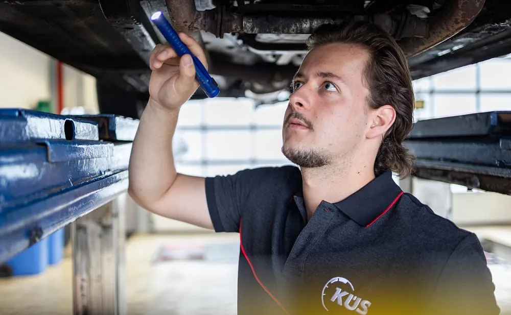 Fahrzeugtechniker beleuchtet den Unterboden eines Autos